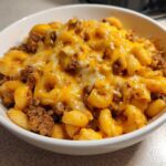 Close-up of a white bowl filled with cheesy, saucy macaroni and ground beef from the cheeseburger casserole.