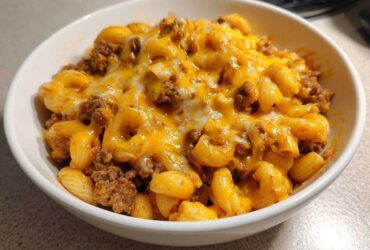 Close-up of a white bowl filled with cheesy, saucy macaroni and ground beef from the cheeseburger casserole.