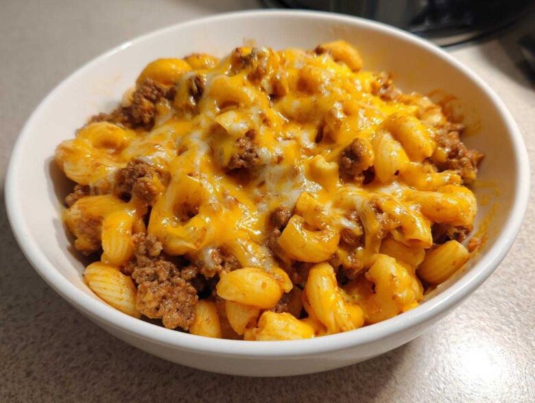 Close-up of a white bowl filled with cheesy, saucy macaroni and ground beef from the cheeseburger casserole.