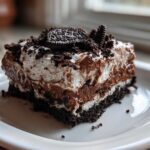 A layered slice of rich chocolate dirt cake with cream, pudding, and Oreo crumbs on a white plate.