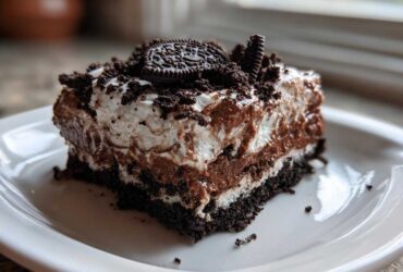 A layered slice of rich chocolate dirt cake with cream, pudding, and Oreo crumbs on a white plate.