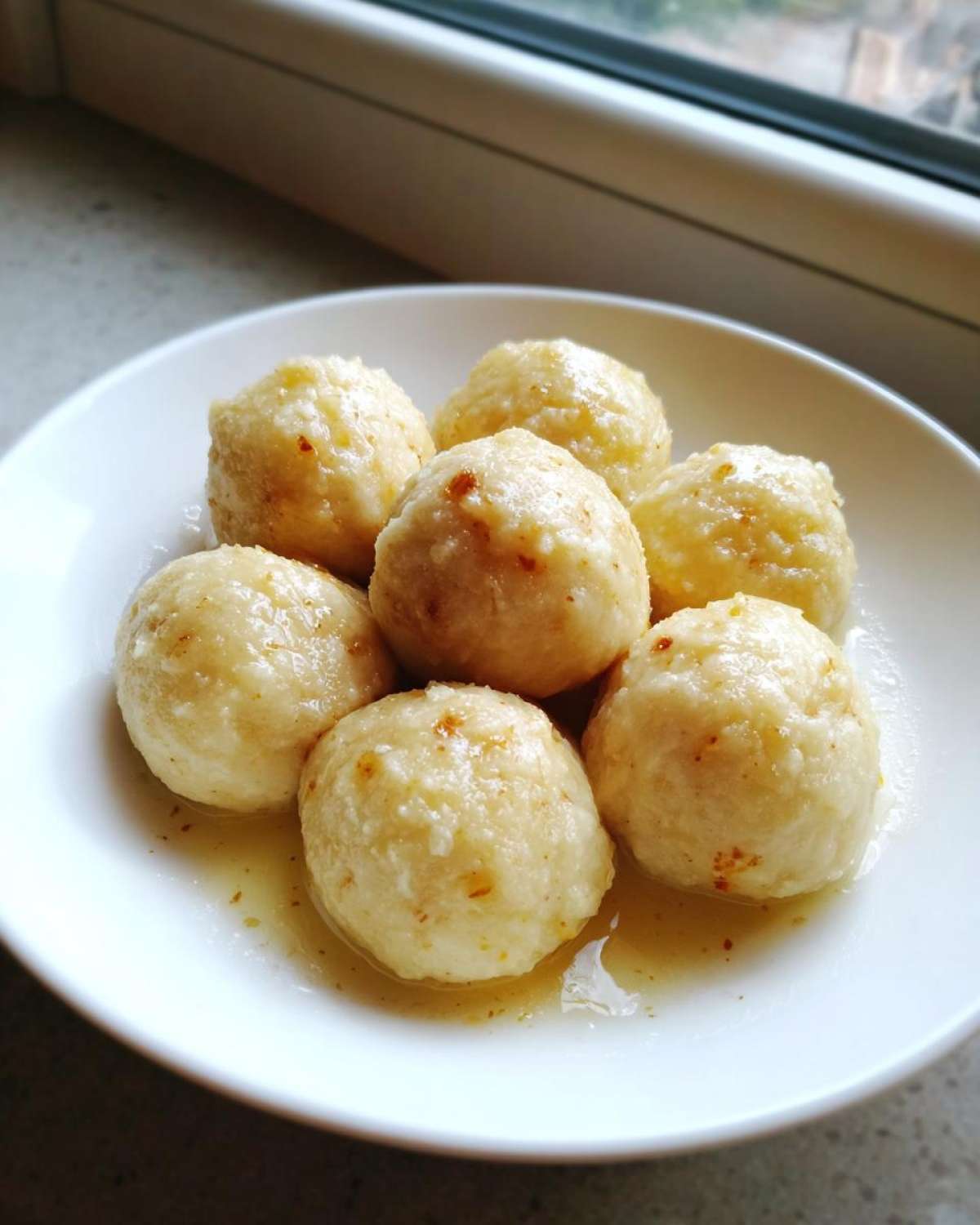 A close-up of seven potato dumplings served in a white bowl with melted butter or sauce.