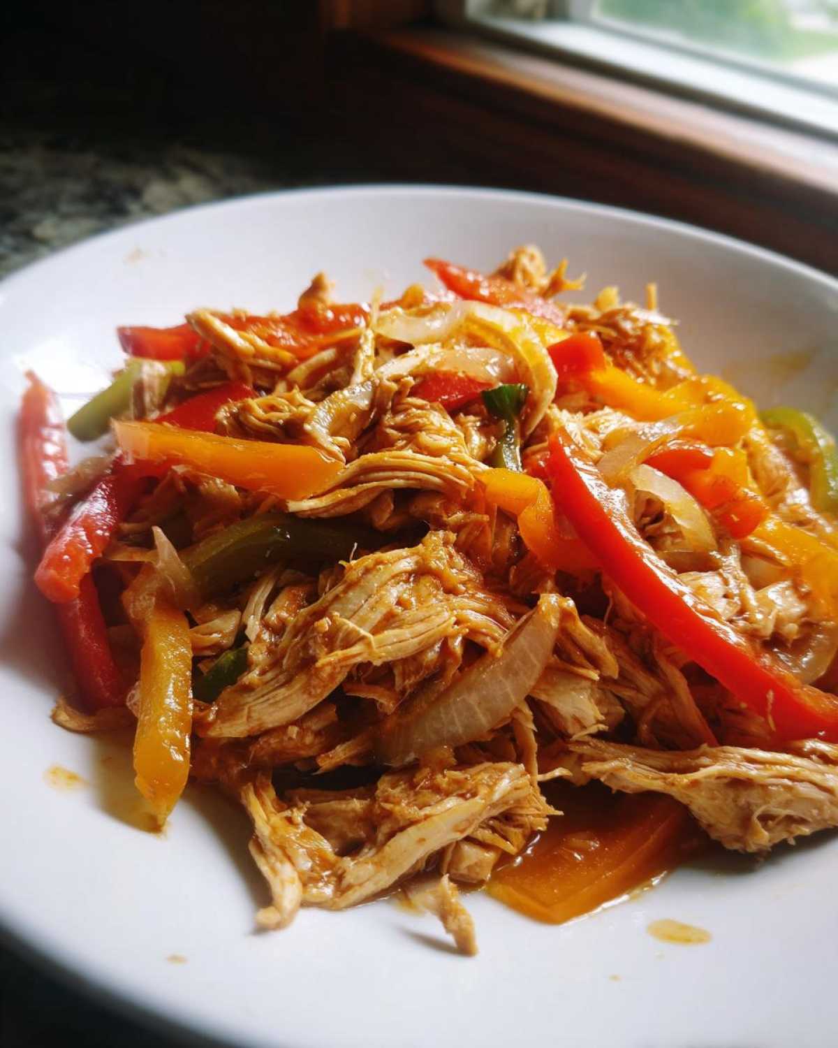 A close-up of shredded chicken mixed with colorful bell peppers and onions, perfect for crockpot chicken fajitas.