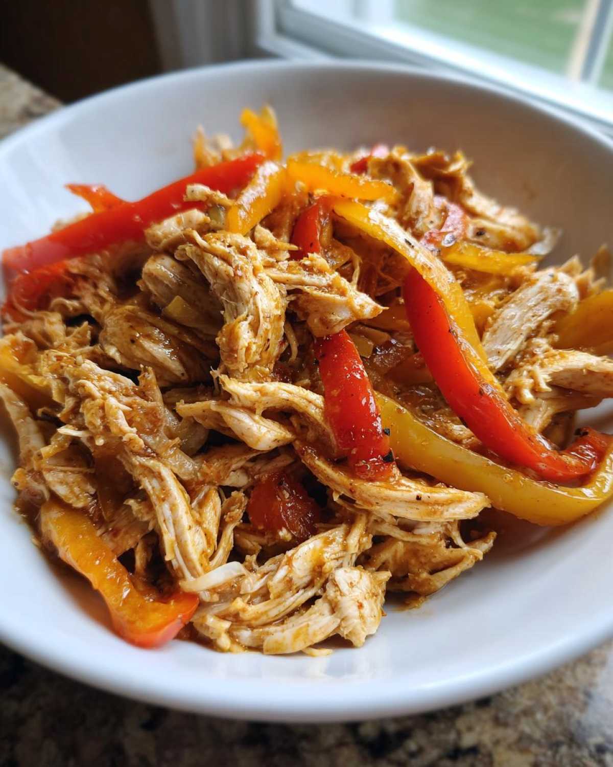 Close-up of shredded chicken mixed with sautéed red and yellow bell peppers for crockpot chicken fajitas.