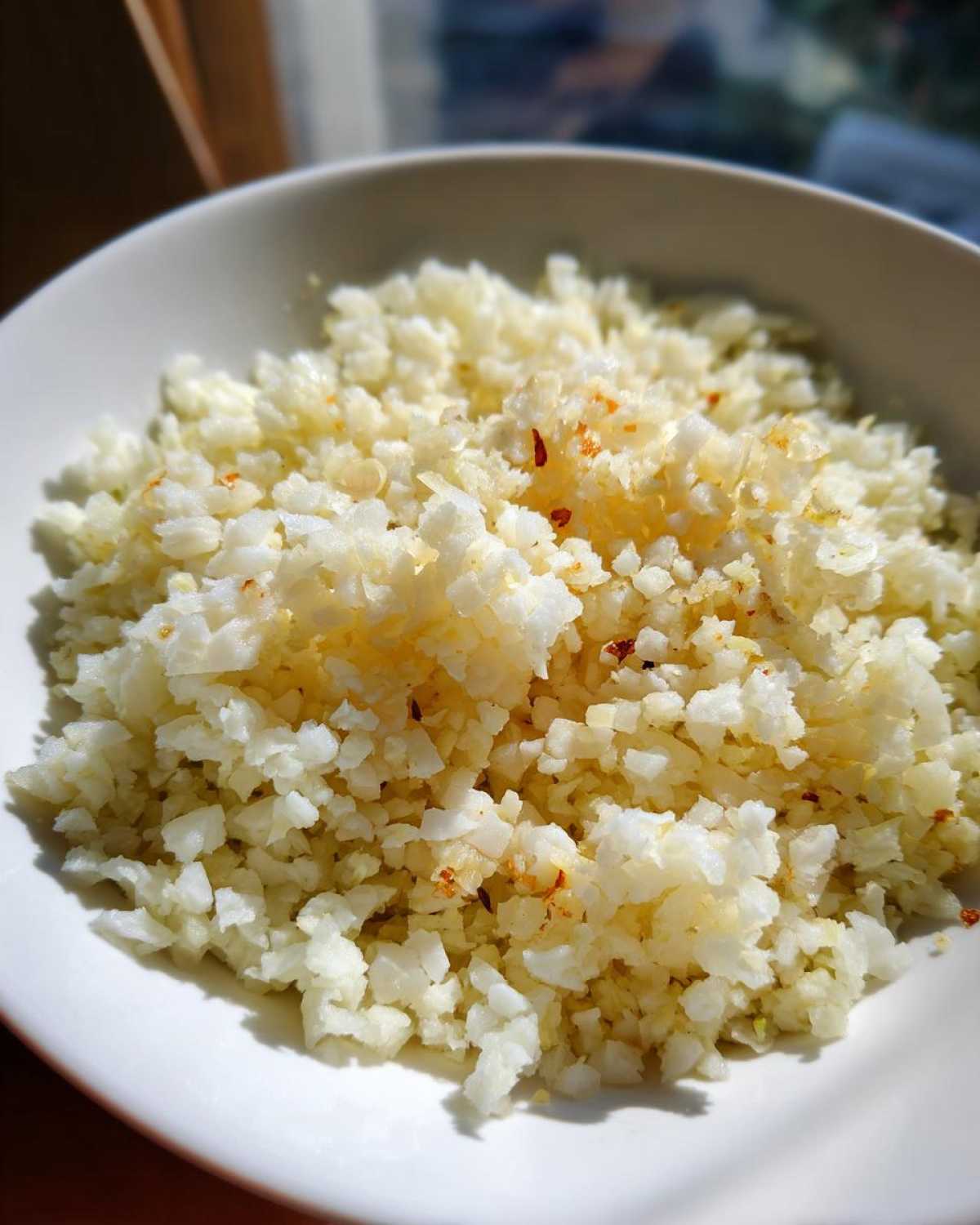 Close-up of fluffy, white cauliflower rice seasoned lightly in a white bowl.