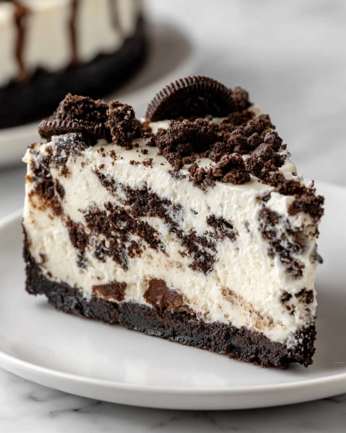 A perfect slice of amazing Oreo cheesecake featuring a dark cookie crust, creamy filling mixed with chocolate chunks, and topped with crumbs and a whole cookie.