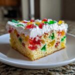 A moist slice of jello poke cake showing colorful gelatin pieces inside a yellow cake base, topped with white frosting.