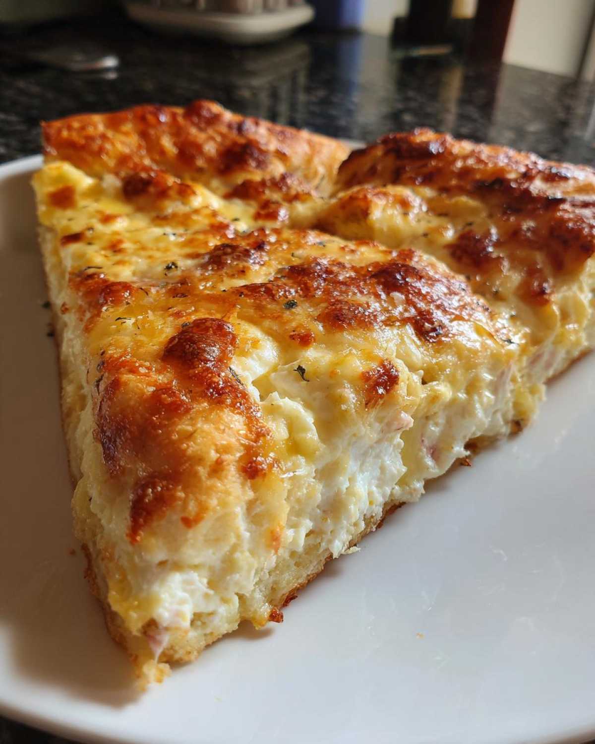 Close-up of a thick slice of white pizza with a creamy ricotta filling and golden-brown, bubbly cheese topping.