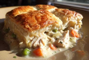 Close-up of a serving of slow cooker chicken pot pie with flaky, golden biscuits over creamy chicken and vegetable filling.