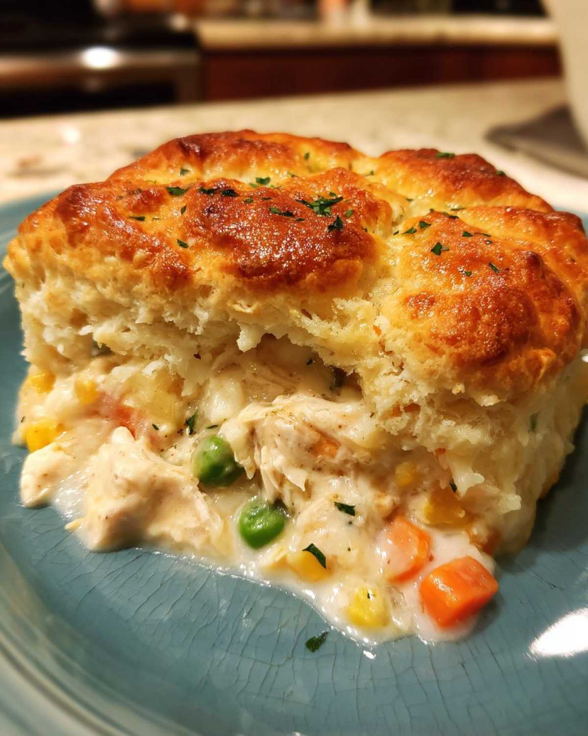 A close-up of a serving of slow cooker chicken pot pie with a golden biscuit topping spilling creamy filling with chicken and vegetables.