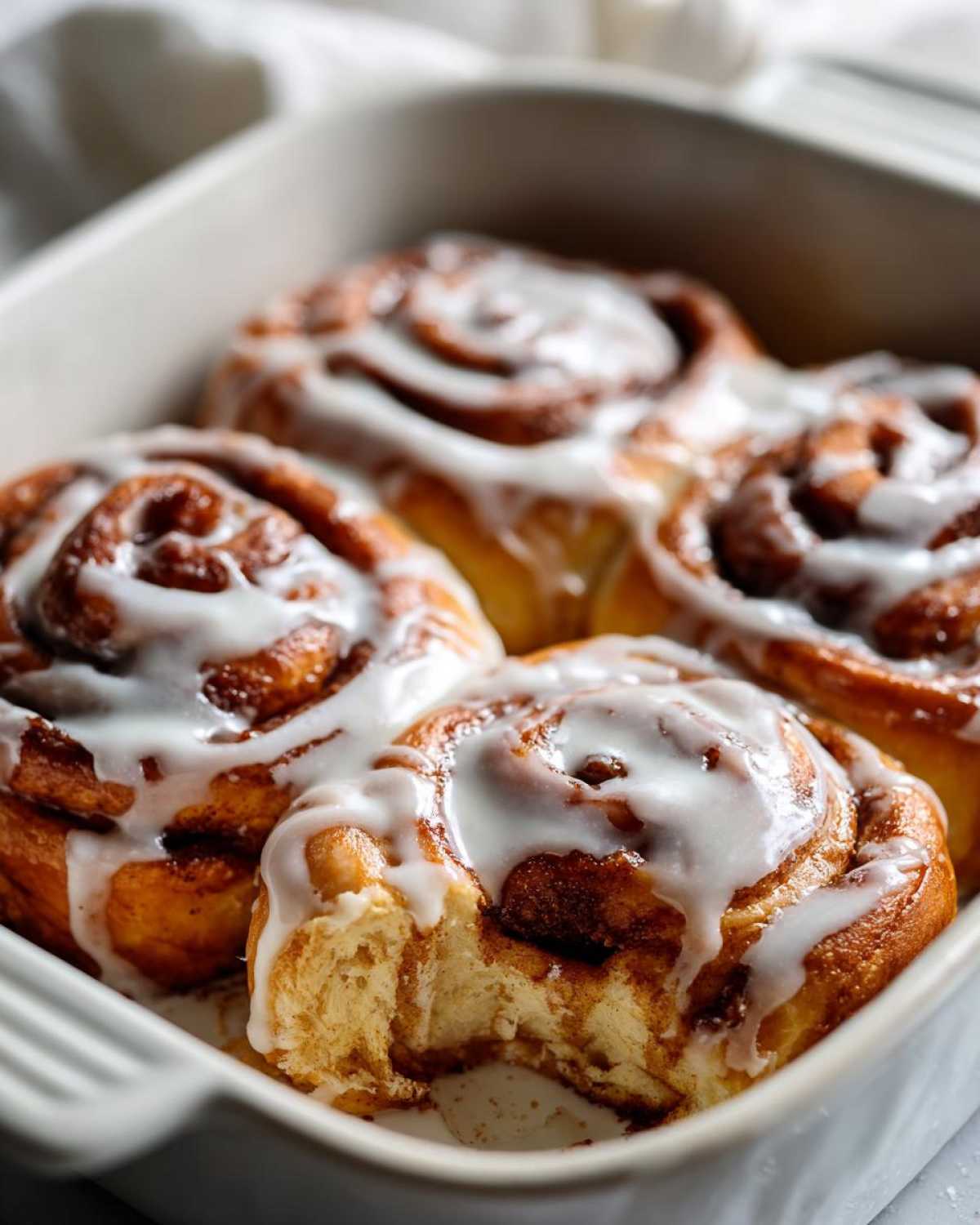 Close-up of four gooey small batch cinnamon rolls topped with white icing in a white baking dish.