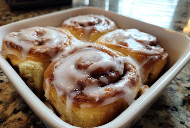 Four freshly baked small batch cinnamon rolls drizzled with thick white icing in a white square baking dish.