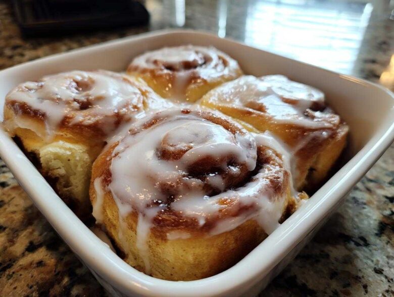 Four freshly baked small batch cinnamon rolls drizzled with thick white icing in a white square baking dish.