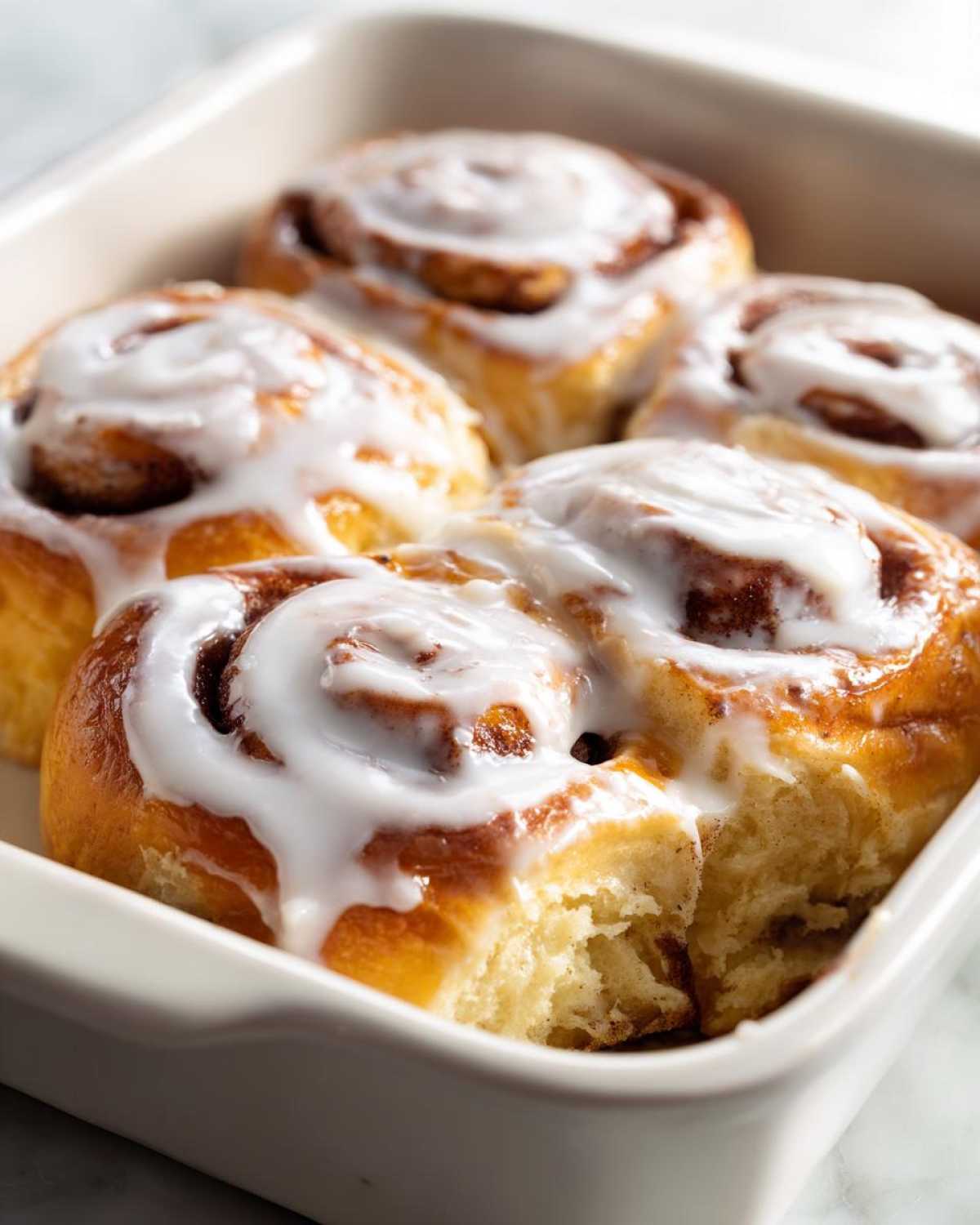 Close-up of four gooey small batch cinnamon rolls topped with thick white icing in a baking dish.