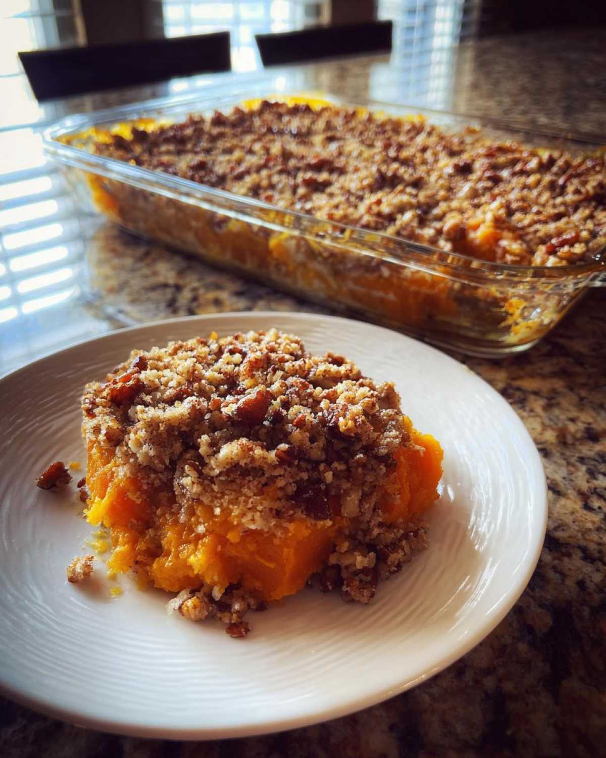 A serving of vibrant orange southern sweet potato casserole topped with a crunchy pecan streusel on a white plate.