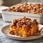 A slice of rich, orange southern sweet potato casserole topped with a crunchy pecan streusel, served on a plate.