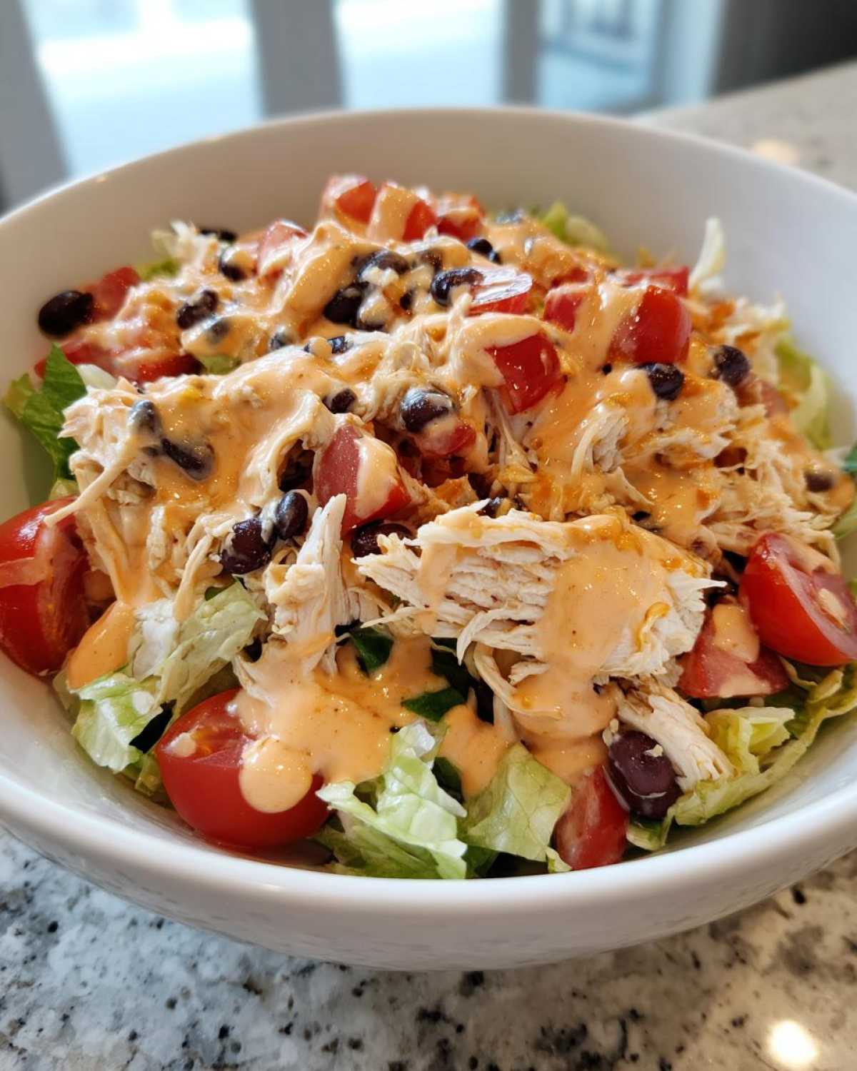 A close-up view of a vibrant southwest chicken salad featuring shredded chicken, black beans, tomatoes, and creamy dressing over lettuce.