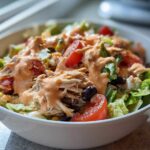 Close-up of a vibrant southwest chicken salad featuring shredded chicken, tomatoes, black beans, and creamy orange dressing.