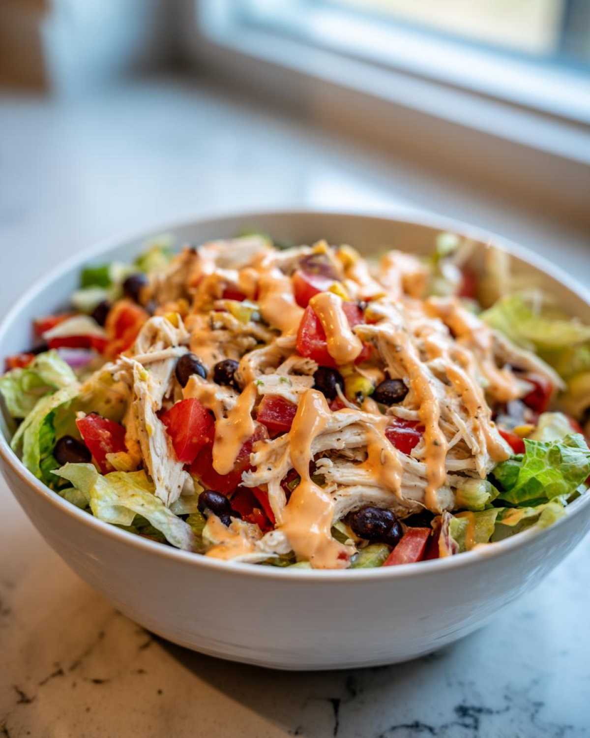 A white bowl filled with southwest chicken salad featuring shredded chicken, black beans, tomatoes, and a creamy orange dressing.