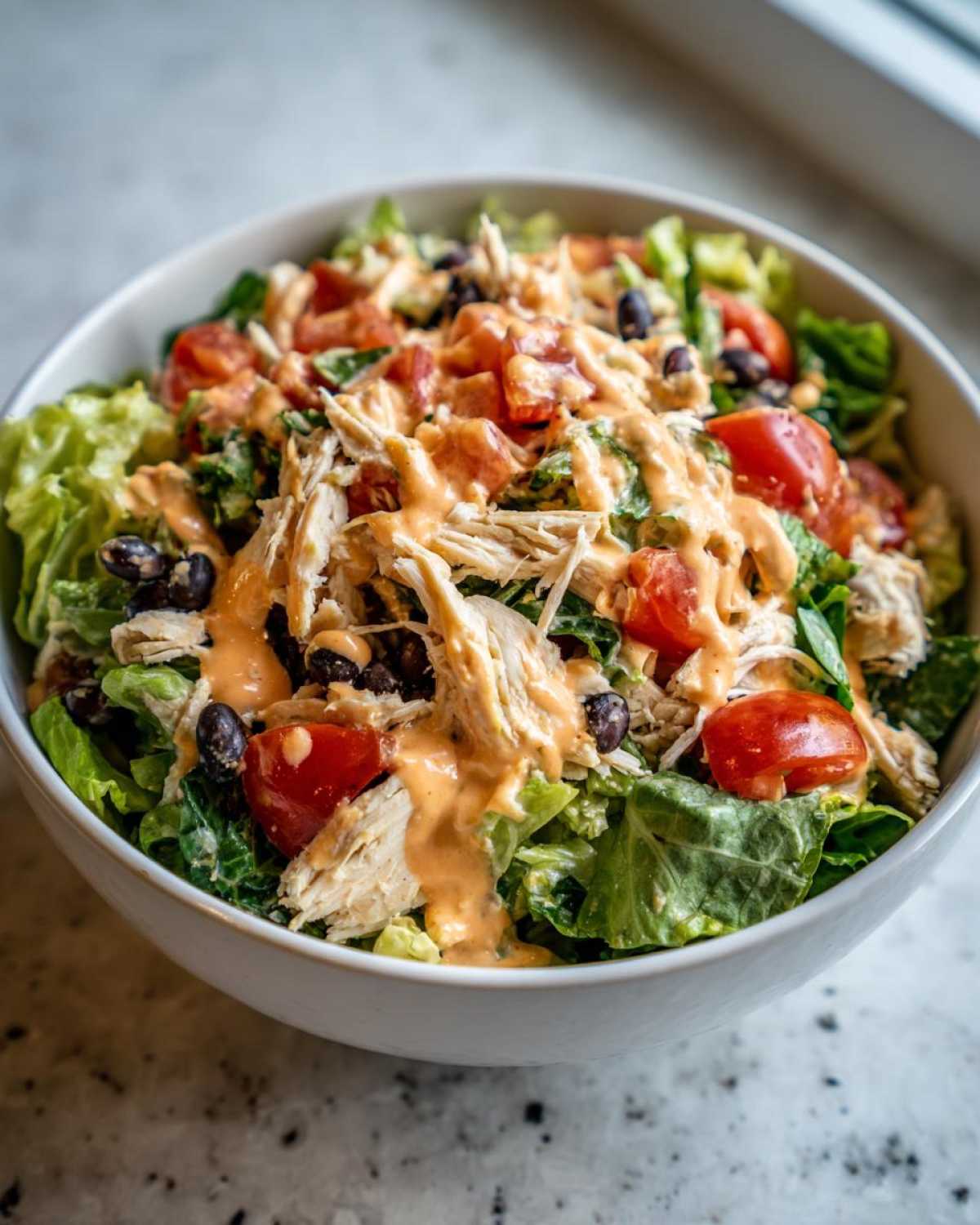 A close-up of a vibrant southwest chicken salad featuring shredded chicken, black beans, tomatoes, and a creamy orange dressing.