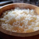 Close-up of perfectly cooked, steaming sushi rice resting in a traditional wooden hangiri bowl.