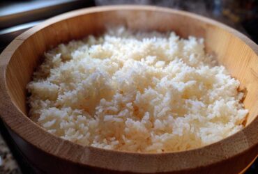 Close-up of perfectly cooked, steaming sushi rice resting in a traditional wooden hangiri bowl.
