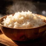 Close-up of perfectly cooked, steaming sushi rice piled high in a wooden bowl.
