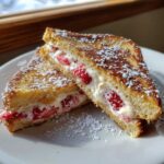 Two halves of golden-brown stuffed french toast filled with cream cheese and strawberries, dusted with powdered sugar.