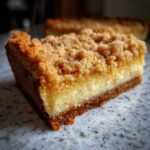Close-up of a rich slice of sugar cookie cheesecake featuring a thick crust, creamy filling, and golden crumb topping.