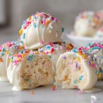 A close-up of white chocolate coated sugar cookie truffles, one cut open showing the soft interior.