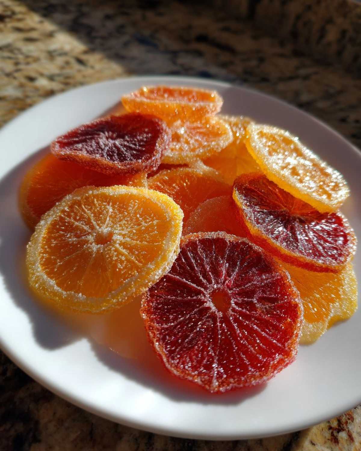 A pile of glistening candied orange slices, including blood orange and regular orange varieties, coated in sugar.