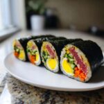 Four thick slices of vibrant tuna kimbap showing layers of tuna, egg, cucumber, and carrots wrapped in nori.