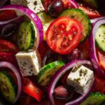 Close-up macro shot of a vibrant greek salad featuring feta cheese cubes, red onion rings, tomato slices, and olives.
