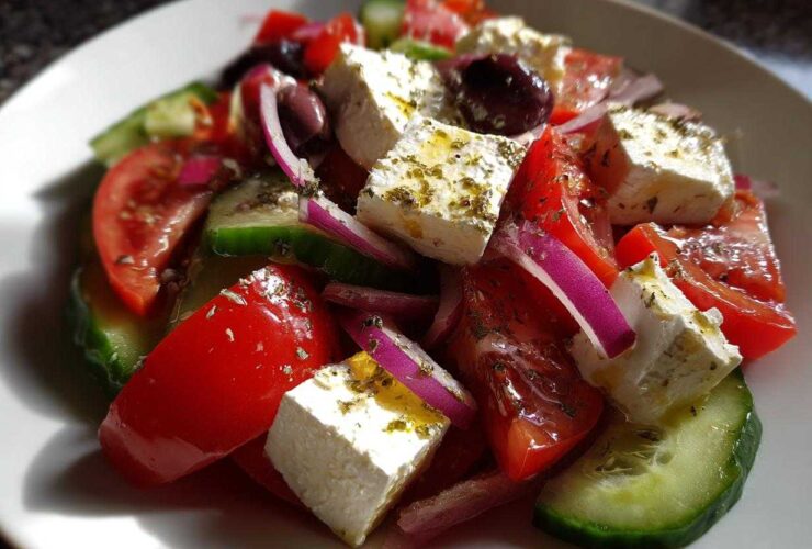 Close-up of a vibrant greek salad featuring large chunks of feta cheese, red tomatoes, cucumber, red onion, and Kalamata olives.