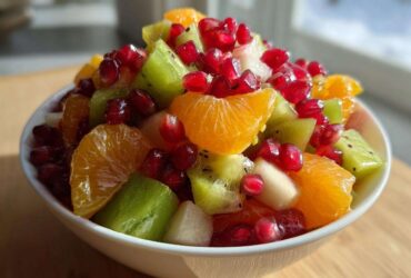 Close-up of a bright winter fruit salad featuring orange segments, green kiwi chunks, and bright red pomegranate seeds in a white bowl.