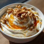 A close-up of a bowl of creamy whipped ricotta dip topped with a drizzle of honey and whole walnuts.