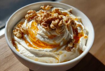 A close-up of a bowl of creamy whipped ricotta dip topped with a drizzle of honey and whole walnuts.