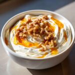 A close-up of creamy whipped ricotta dip topped with candied walnuts and a drizzle of honey or caramel.