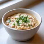 A close-up of a white bowl filled with creamy white chicken chili, topped with melted cheese and fresh cilantro.