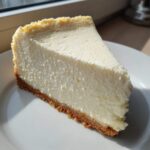 A thick, creamy slice of white chocolate cheesecake with a graham cracker crust on a white plate.
