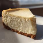 A perfect slice of creamy white chocolate cheesecake with a thick graham cracker crust, served on a white plate.