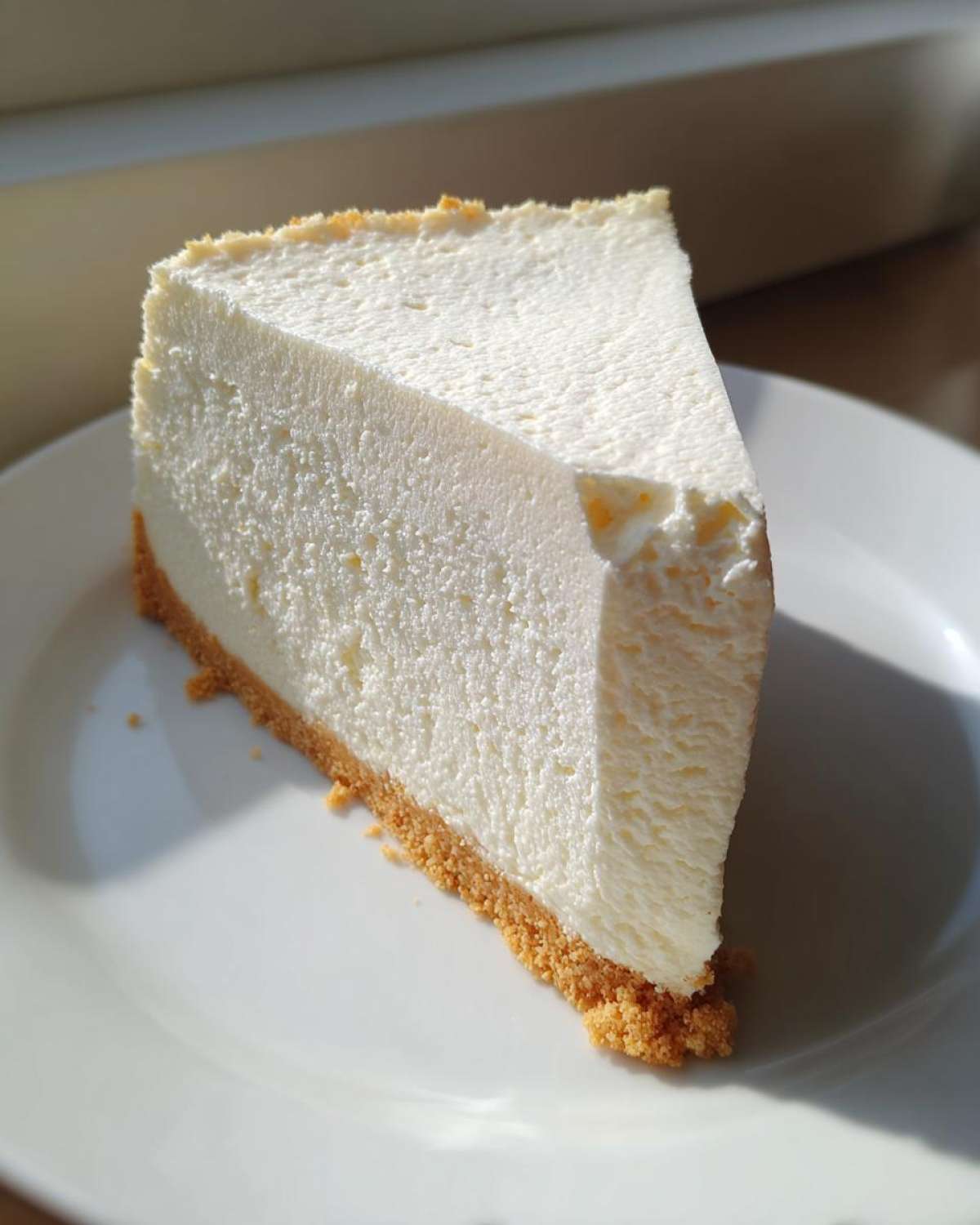 A thick, creamy slice of white chocolate cheesecake with a golden graham cracker crust on a white plate.