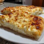 Two slices of thick-crust white pizza topped with melted, browned cheese served on a white plate.
