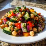 A vibrant, close-up serving of zesty bean salad featuring chickpeas, cucumber, red onion, and peppers.