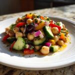 A vibrant serving of zesty bean salad featuring chickpeas, cucumber, red onion, and bell peppers on a white plate.