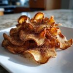 A close-up of crispy Air Fryer Cinnamon Sugar Apple Chips piled high on a white plate, glistening with sugar.