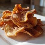A pile of crispy, golden Air Fryer Cinnamon Sugar Apple Chips dusted heavily with cinnamon sugar on a white plate.