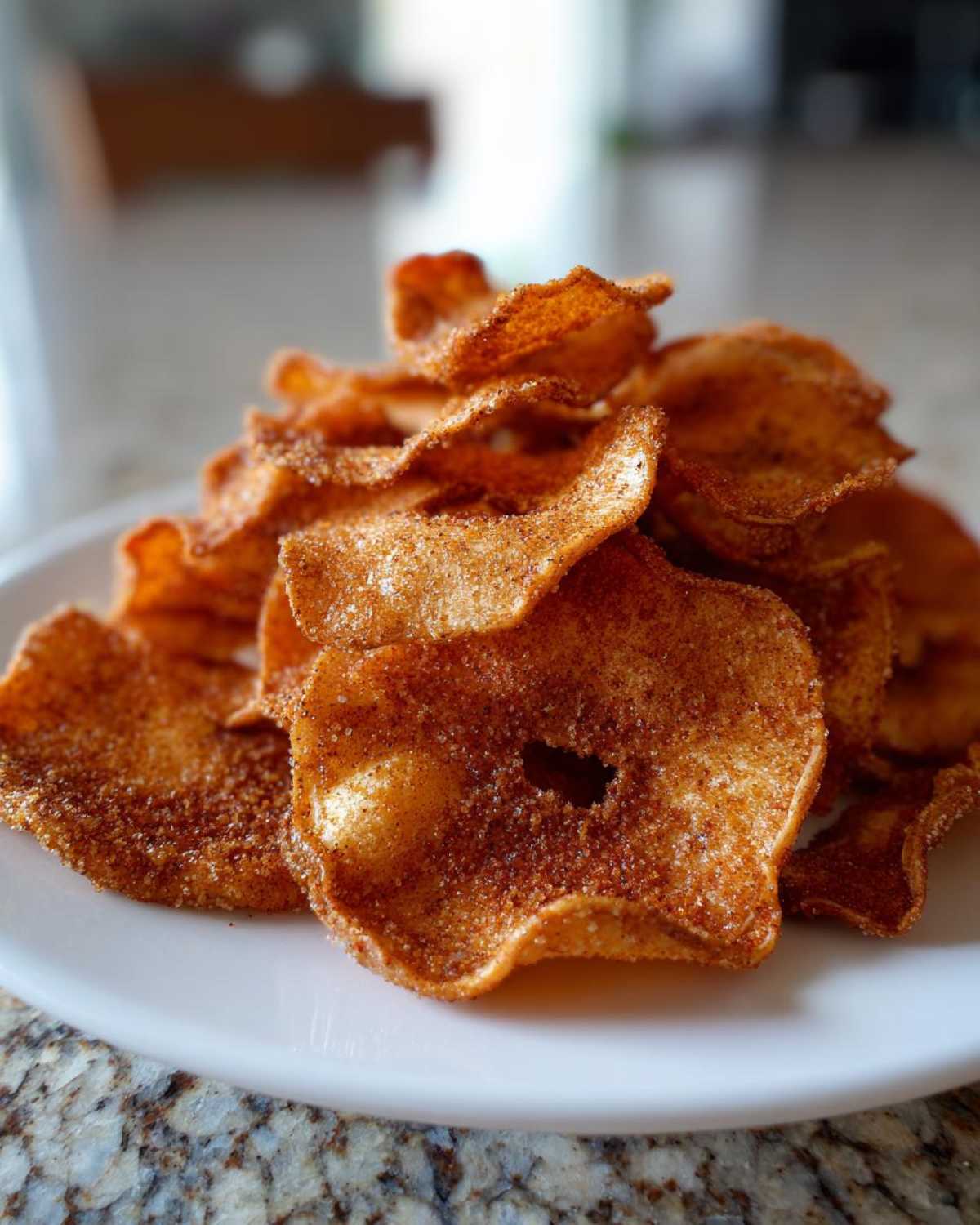 A close-up pile of crispy Air Fryer Cinnamon Sugar Apple Chips dusted heavily with cinnamon sugar.