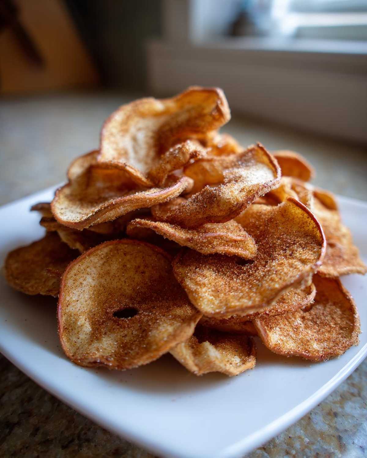 A close-up shot of a pile of crispy Air Fryer Cinnamon Sugar Apple Chips dusted heavily with cinnamon.