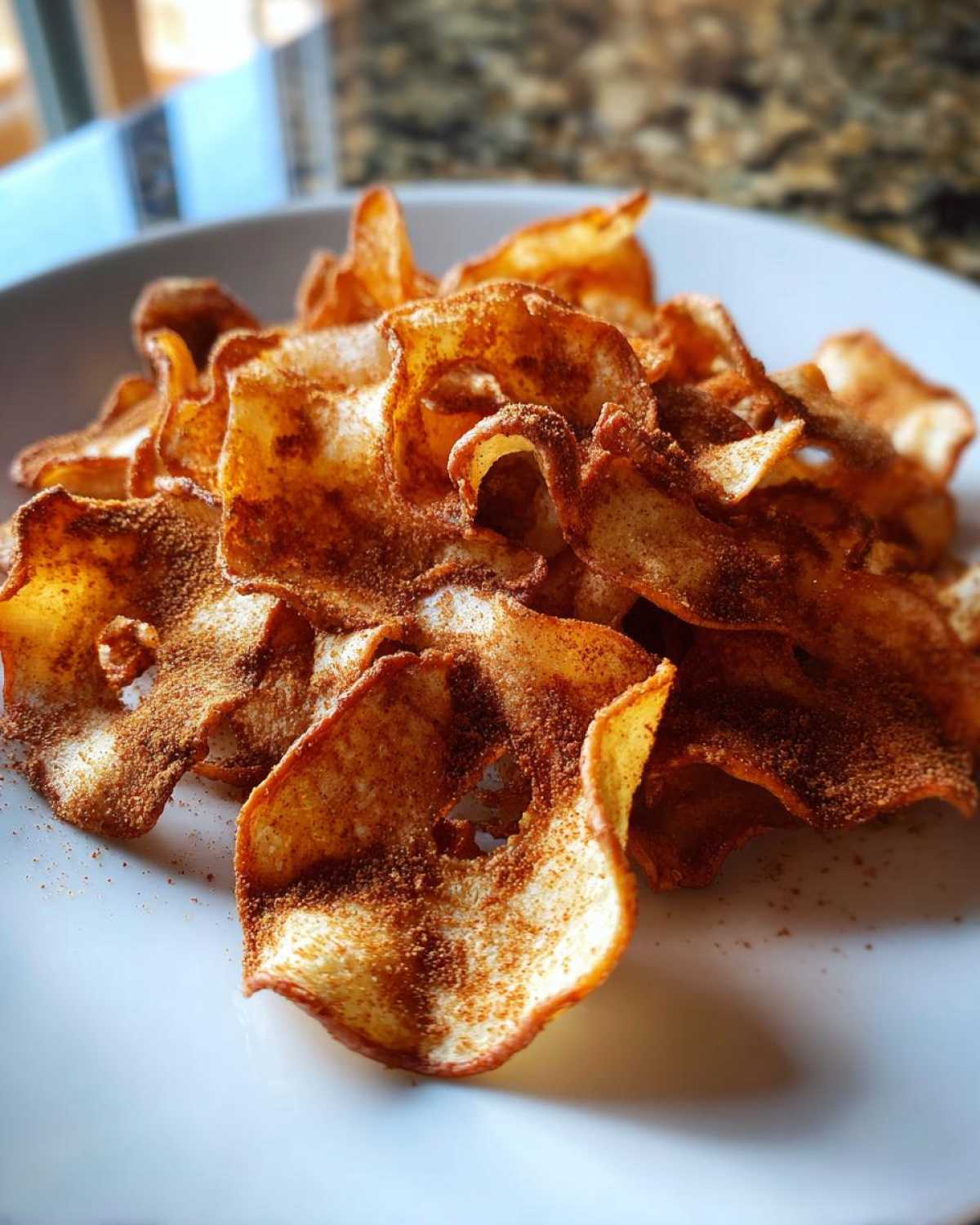 A close-up of crispy Air Fryer Cinnamon Sugar Apple Chips piled on a white plate, heavily dusted with cinnamon.